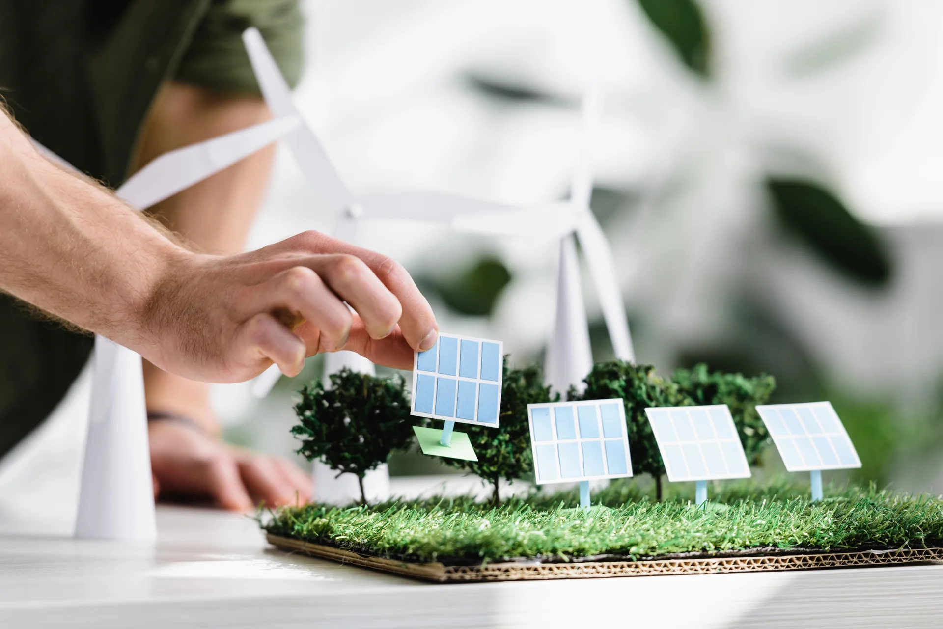 Hand placing miniature solar panel on green renewable energy model